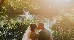 Bride and groom kissing by lake with fountain