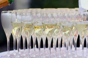 Many champagne flute glasses filled with champagne and bubbling standing very close together on a white table.