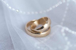 Two stacked wedding rings with decoration of veil and pearls beneath.