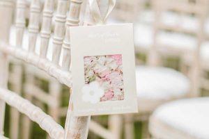 White wooden chairs with padded seats and rail backs and a sachet of flower petals hanging from the back left.